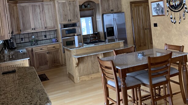 A spacious kitchen with wooden cabinets, a central island, and a dining area with chairs. - Romantic hideaway on the lake nestled in the pines 79 miles north of Pittsburgh. (Ringgold)