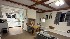 A living room with a gray sofa, a wooden dining table with chairs, a ceiling fan, and a kitchen in the background.