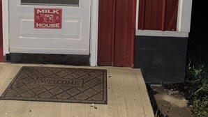 A white door with a window, a 'Milk House' sign, a 'Welcome' mat, and a street sign reading 'Milk Parlor.'