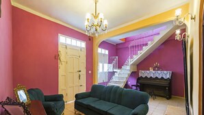 Ein Wohnzimmer mit einem grünen Sofa, einem Klavier und einer Treppe, deren Wände violett sind.