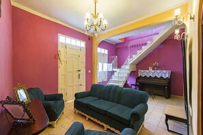A living room with a green sofa, a piano, and a staircase with purple walls. - Hostal Casa Reguera (Trinidad)