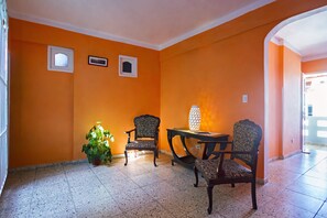 A room with orange walls, two chairs, a table, and a potted plant. - Hostal Casa Reguera (Trinidad)