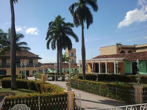 A courtyard with palm trees, a fountain, and buildings with tiled roofs. - Hostal Casa Reguera (Trinidad)