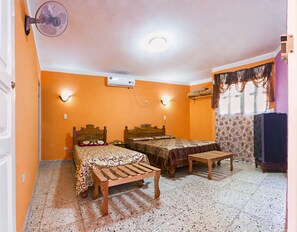 A room with two beds, a wooden bench, a fan, and an air conditioning unit. - Hostal Casa Reguera (Trinidad)