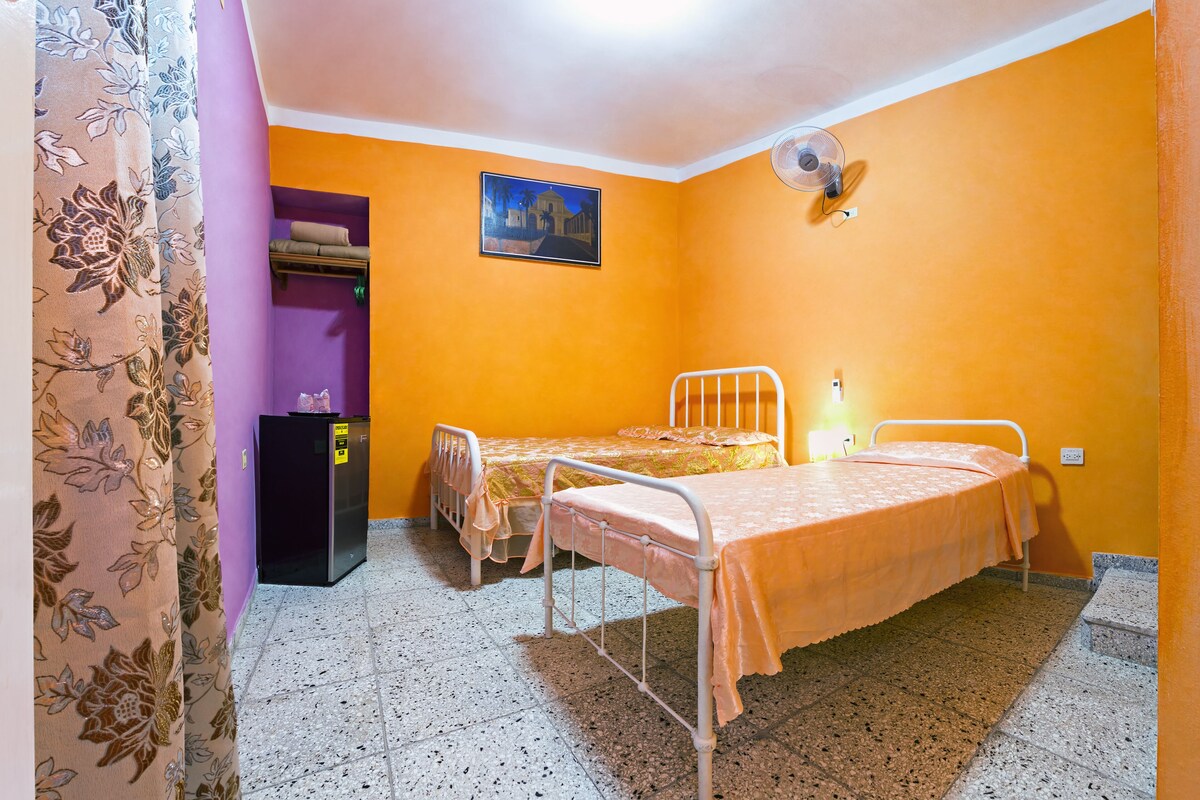 A small room with two beds, a refrigerator, and a picture on the wall.
