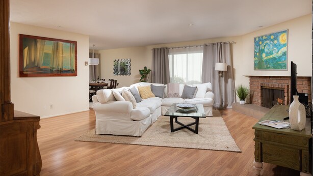 A living room with a sectional sofa, a glass coffee table, a fireplace, and artwork on the walls.