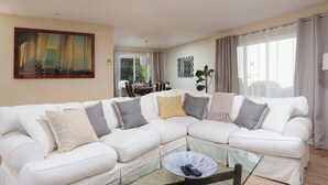 A living room with a white sectional sofa, a glass coffee table, and a painting on the wall.