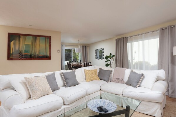Ein Wohnzimmer mit einem weißen Ecksofa, einem Glastisch und einem Bild an der Wand.
