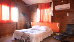 Une pièce de type cabane en bois, comprenant un lit, une chaise et un appareil de climatisation.
