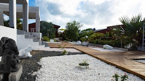 Un espace extérieur moderne doté d’une terrasse en bois, de galets blancs et de différentes plantes.