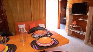 A dining area with a wooden table set for four, a sofa with cushions, and a television on a wooden shelf.