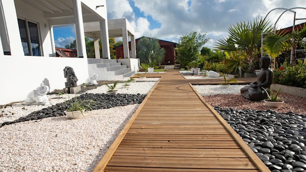Un chemin en bois mène à un bâtiment à la façade blanche et au toit rouge.