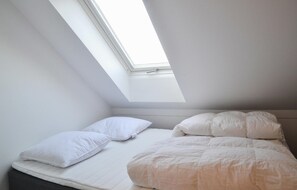 Cozy retreat with a sloped ceiling and natural light pouring in through the skylight, featuring a comfortable bed and matching bedding.