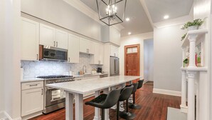 A modern kitchen with white cabinetry, a large island with bar stools, stainless steel appliances, and a hexagonal tile backsplash. - Historic Mini-Mansion on Canal St. Walk to (New Orleans)