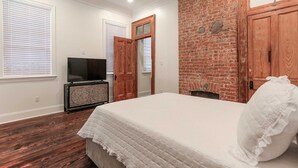 A bedroom with a large bed, a television on a cabinet, and a brick wall. - Historic Mini-Mansion on Canal St. Walk to (New Orleans)