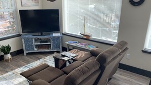 A living room with a brown sofa, a flat-screen TV, a small table with books, and a plant. - New Montana Modern Cottage overlooking Flathead Lake (Somers)