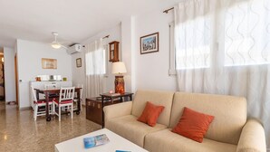 Uma sala de estar com um sofá bege, uma mesa de centro branca e um espaço de refeições com mesa e cadeiras.