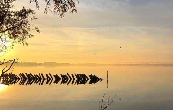A calm lake with a row of wooden stakes in the foreground and a clear sky.