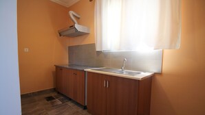 A small kitchen with wooden cabinets, a sink, and a window with curtains. - Jericho rooms (Sarandë)