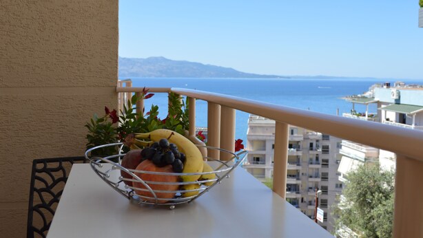 A balcony with a table holding a fruit basket, overlooking a coastal view with buildings and mountains in the distance. - Jericho rooms (Sarandë)