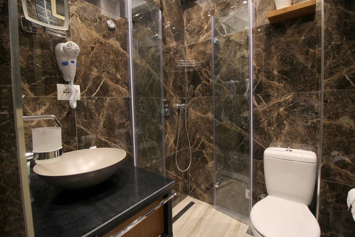 A bathroom with a marble sink, a hairdryer, a glass shower enclosure, and a toilet.