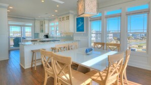 Una cocina amplia con una isla central, sillas de madera y ventanas grandes que ofrecen vistas al exterior.