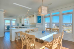 A spacious kitchen with a central island, wooden chairs, and large windows offering a view of the outside.