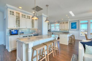 A spacious kitchen with white cabinetry, a large island with stools, and pendant lighting.