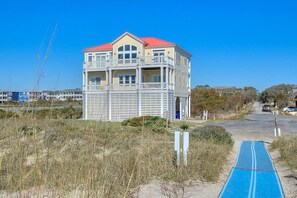 Un immeuble de deux étages, avec un toit rouge et des balcons blancs, situé près d’une plage, le long d’un sentier bleu.