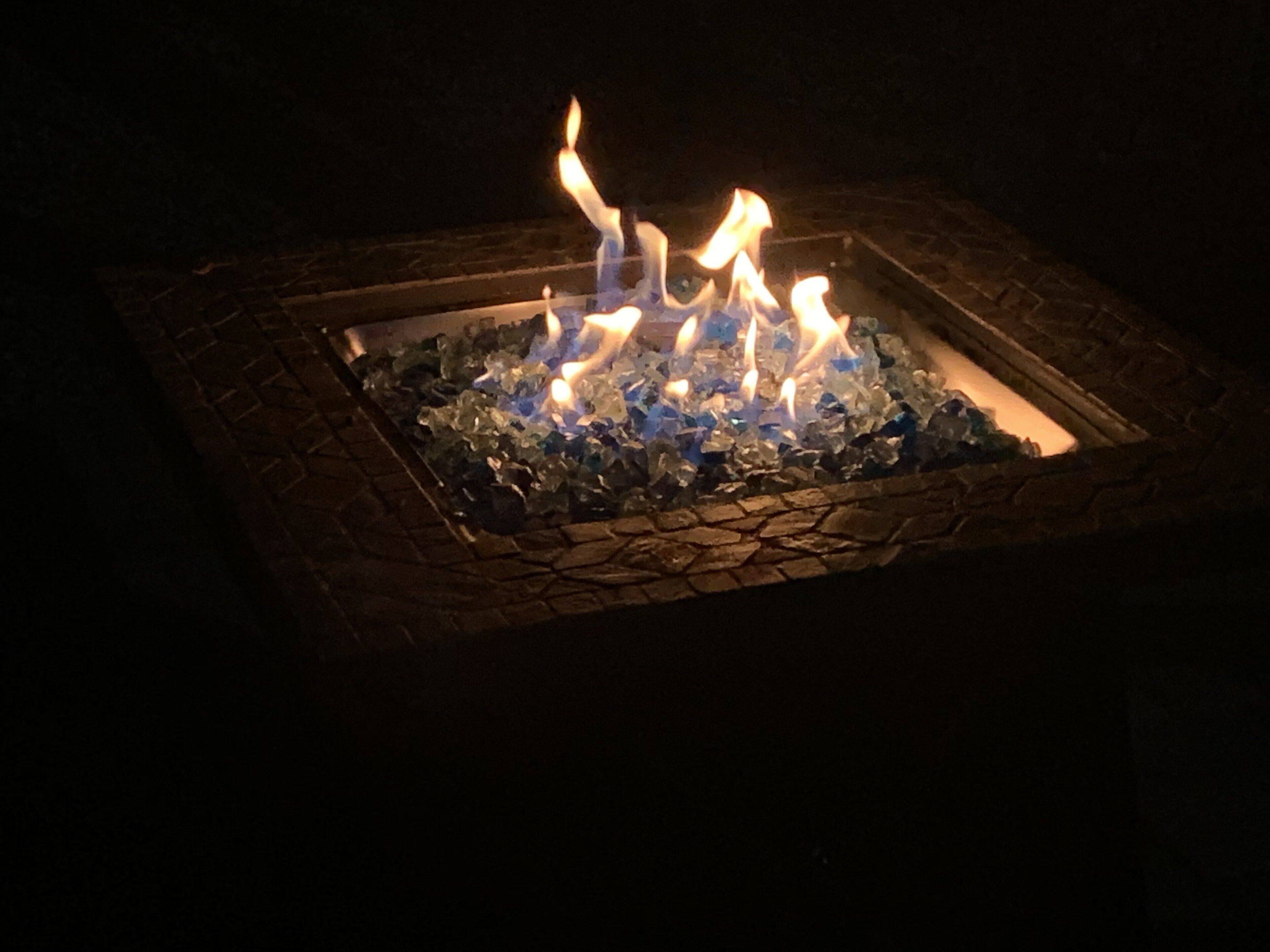 Un foyer carré, bordé de pierres, dans lequel brûlent des flammes.