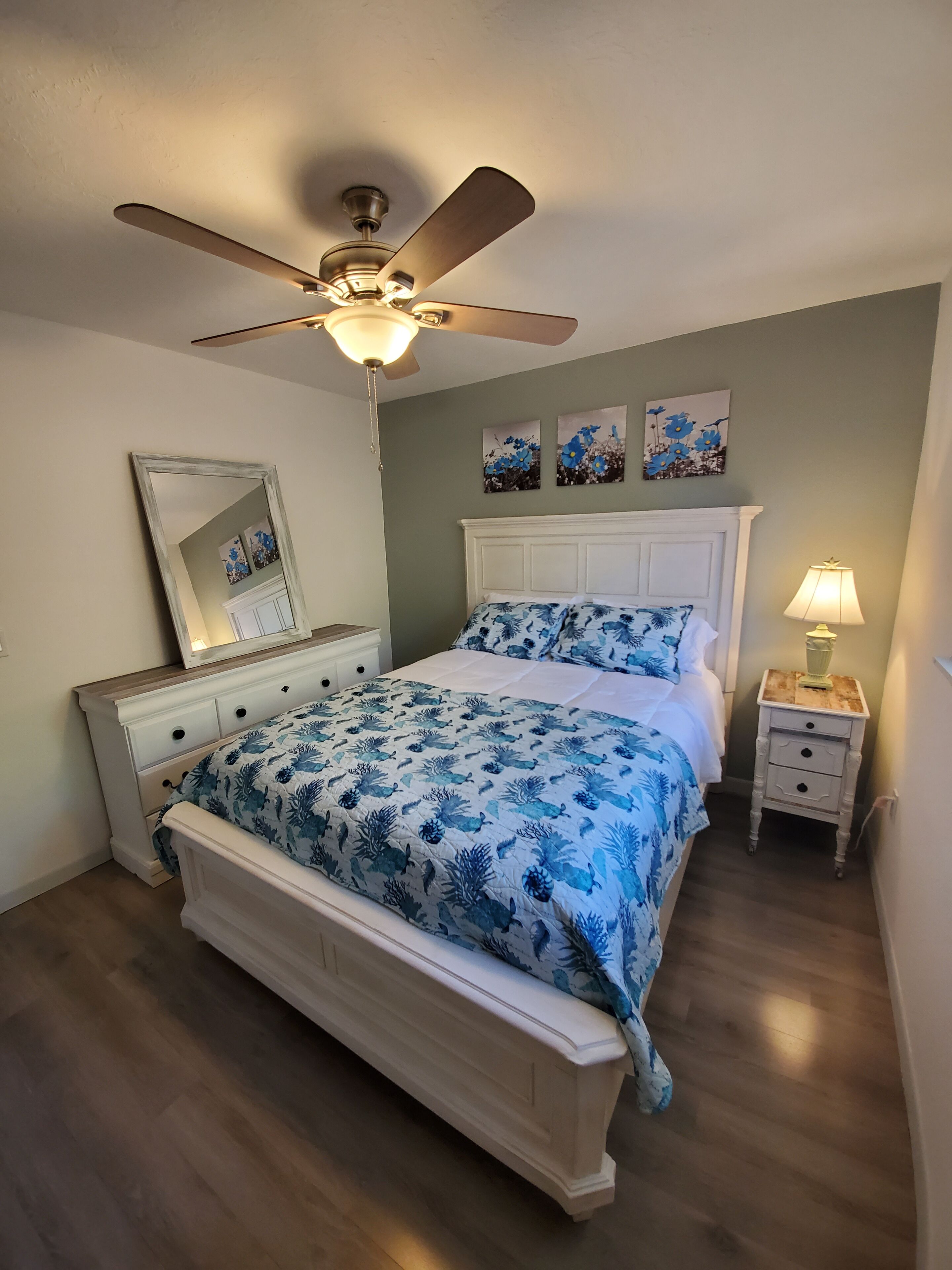Une chambre à coucher avec un lit, une table de chevet, un ventilateur de plafond et des œuvres d’art accrochées au mur.