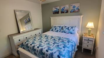 Une chambre à coucher avec un lit, une table de chevet, un ventilateur de plafond et des œuvres d’art accrochées au mur.