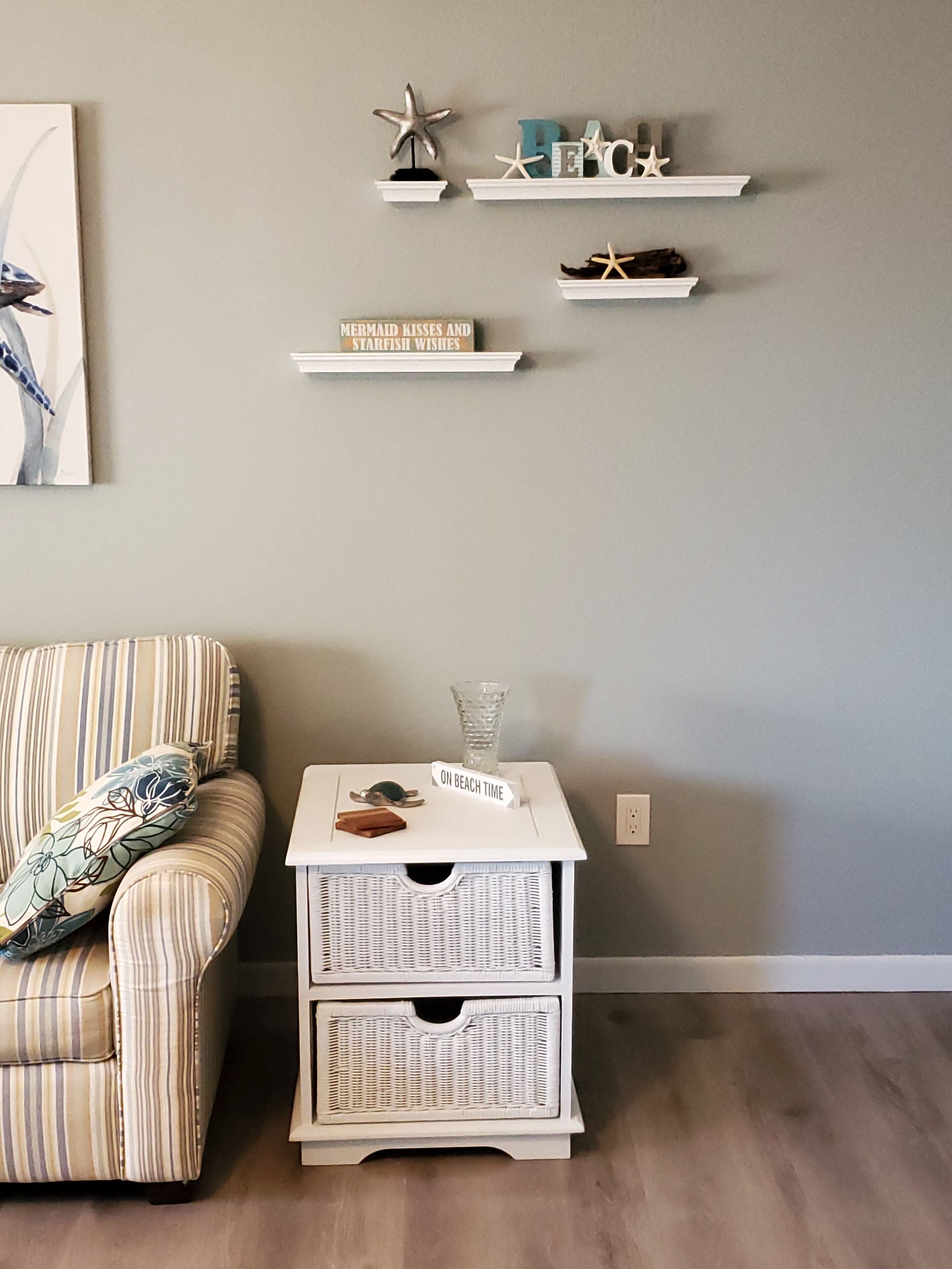 Een kamer met een gestreepte fauteuil, een kleine tafel met een glazen vaas, en een wandplank met decoratieve objecten.