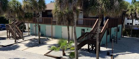 A building with a staircase and palm trees, surrounded by a gravel area.