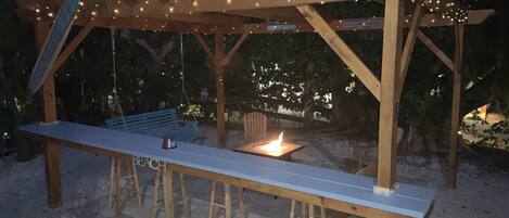 A wooden pergola with string lights, a bench, and a fire pit.