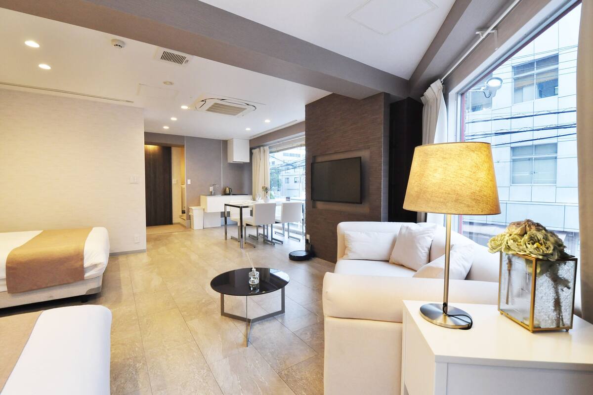 A modern hotel room with a sofa, a coffee table, a lamp, and a TV.