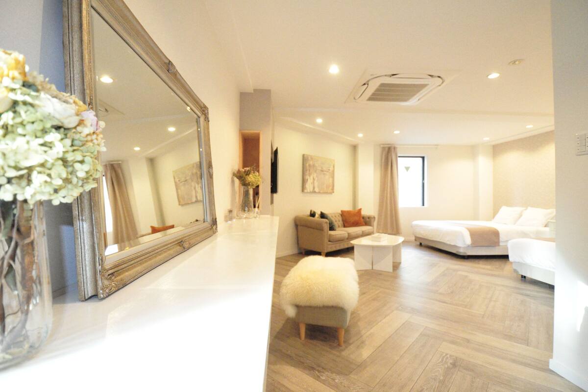 A modern living room with a large mirror, a sofa, a small table, and a fluffy ottoman.