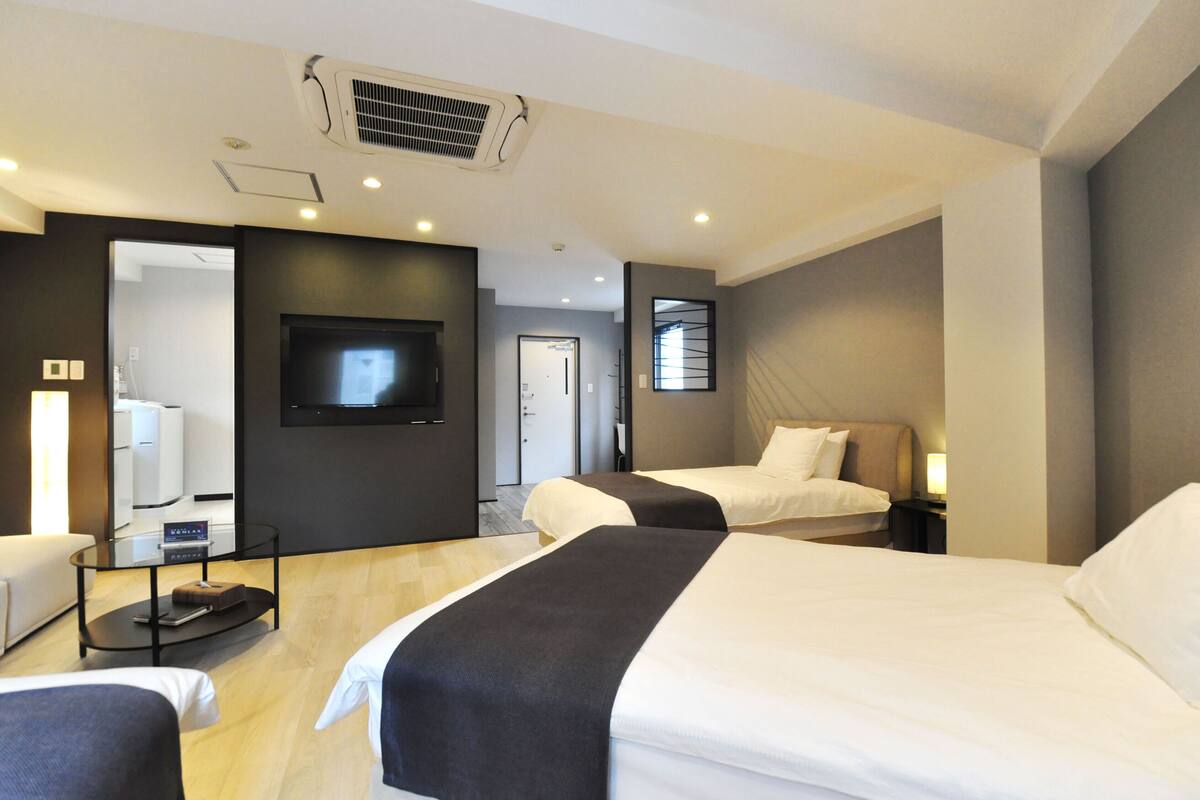 A hotel room with two beds, a TV, a desk with a chair, and a mirror.