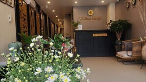 A hotel reception area with a reception desk, a reception sign, a clock, and a plant. - Teamo Hotel (Hai Phong)