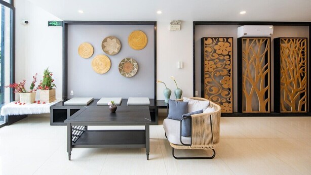 A modern reception area with a dark wooden reception desk, a wicker sofa, and decorative wall art. - Teamo Hotel (Hai Phong)