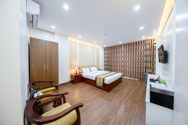 Habitación de hotel con cama, armario de madera, escritorio, silla y televisión en la pared.