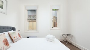 A bedroom with a bed, two windows, a radiator, and a chair.