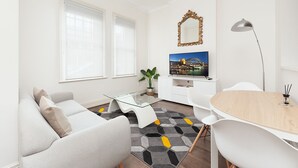 A modern living room with a sofa, coffee table, TV, and dining area.