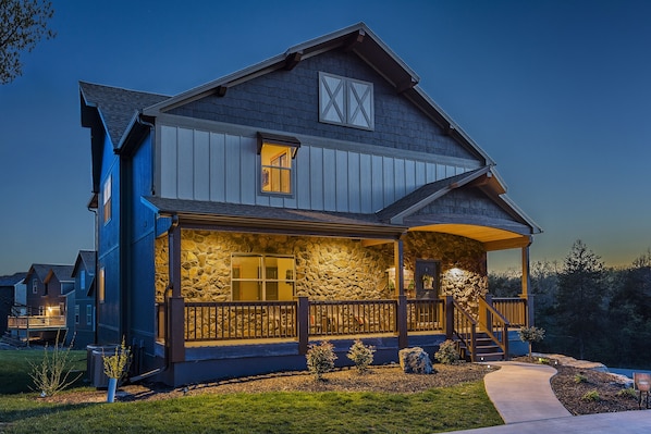 A two-story house with a stone facade, wooden porch, and a small garden.