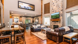 A spacious living area with a stone fireplace, leather furniture, and a large TV mounted on the wall. - THEATER/GAME ROOM w/100” Screen!! Pool Table!  Dining Seats 20! 3 Living Areas! (Hollister)