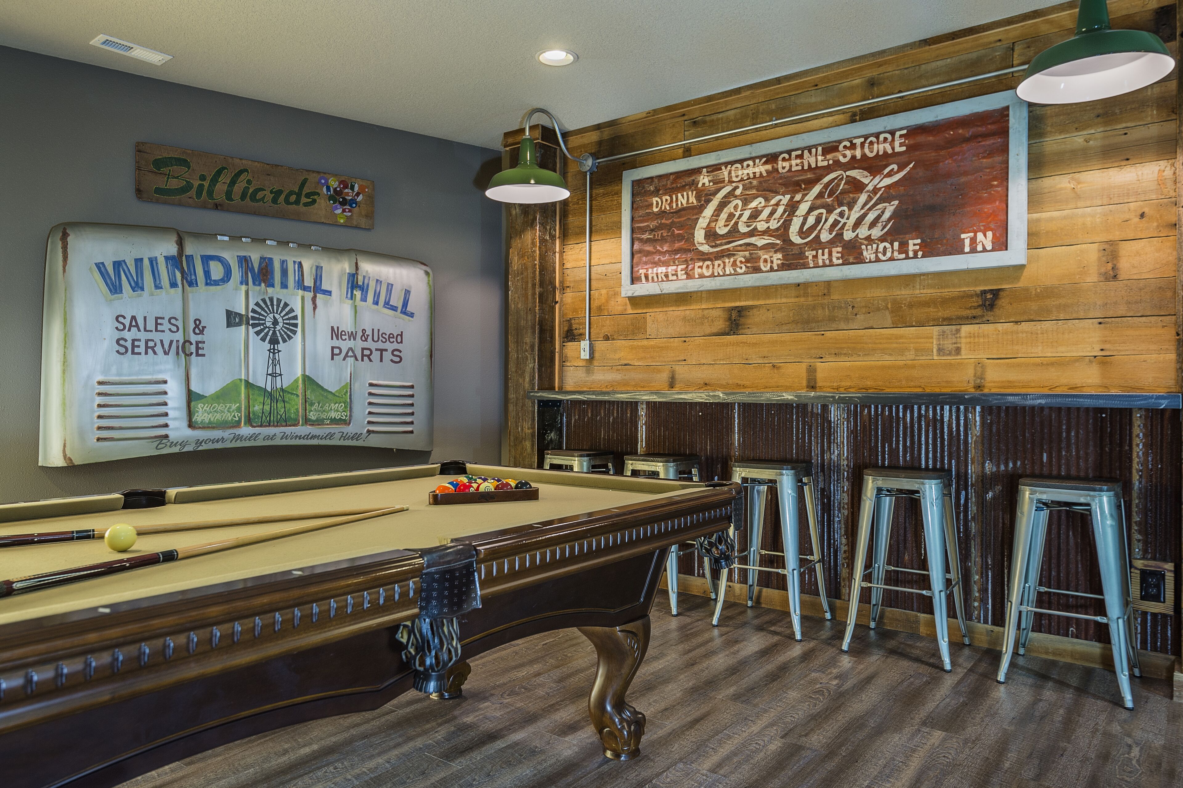 A billiards table with cues and balls, a pool table, and a bar area with stools.
