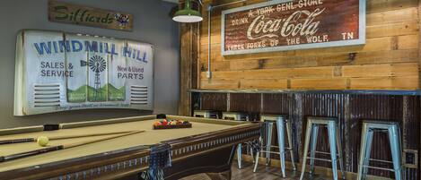 A billiards table with cues and balls, a pool table, and a bar area with stools.