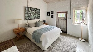 A bedroom with a bed, a nightstand, a lamp, a ceiling fan, a window, and a door. - The Kings Stables at Burnside (Burnside)