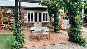 A patio with a table and chairs, a pergola, and a stone building with shutters. - The Kings Stables at Burnside (Burnside)