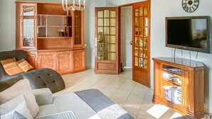A living room with a large TV, a bookshelf, and a sofa with cushions. - Stunning home in Orange (Orange)
